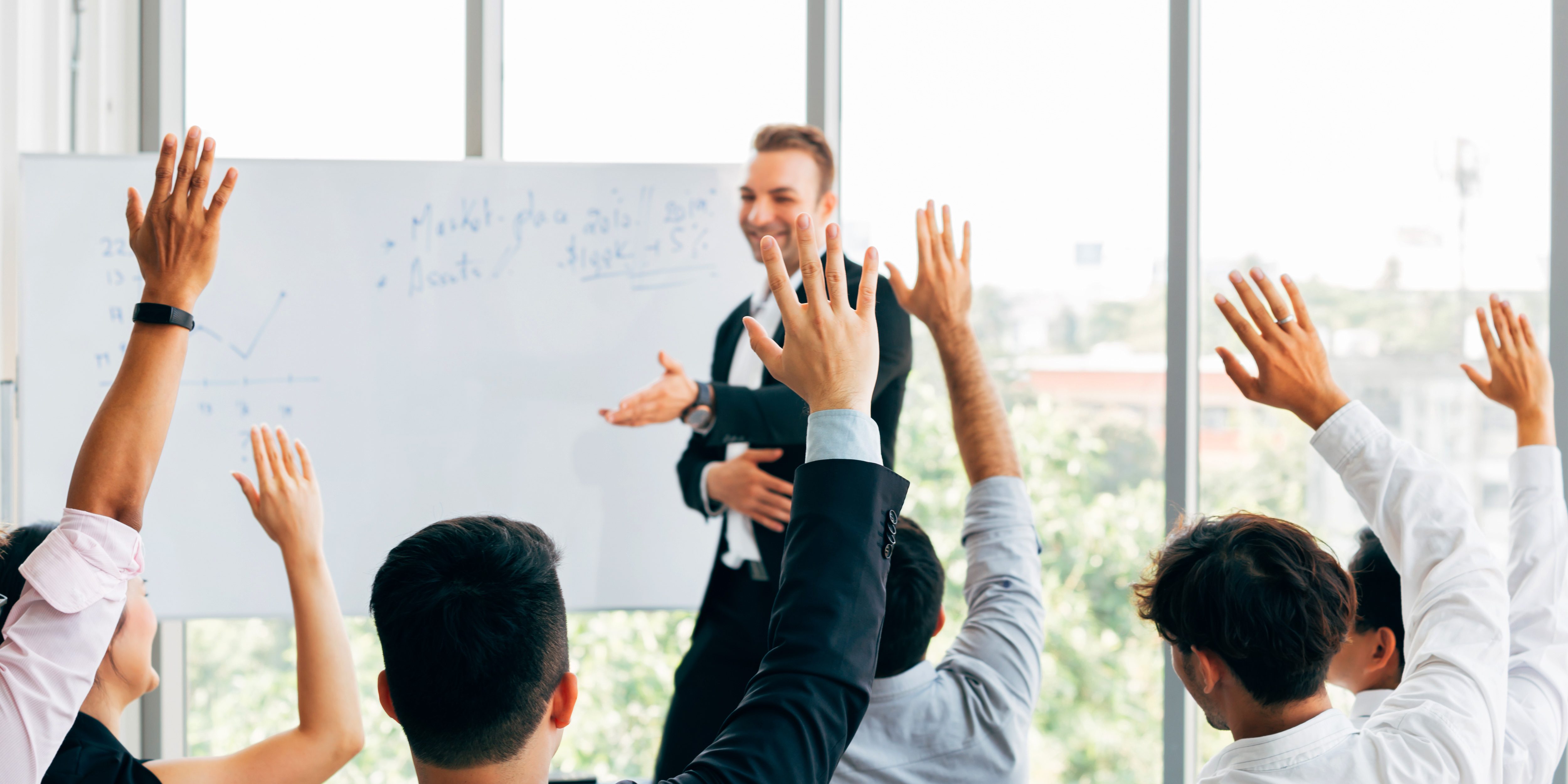 Many business people participants raising up their hand in business seminar conference event inside corporate company office with speaker in front